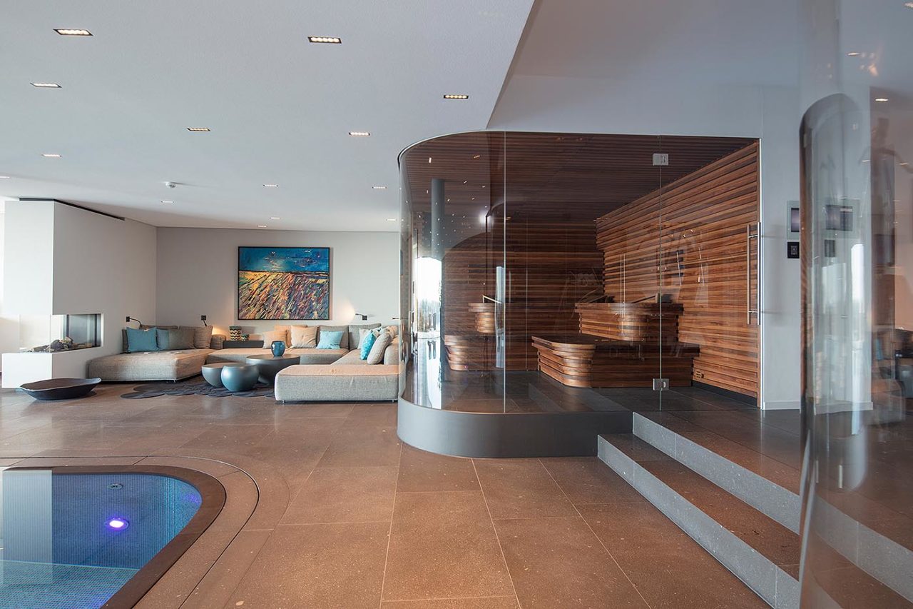 Luxus Sauna | Premium Sauna 6 Luxus Sauna mit gerundeter Glasfront im Private Spa Bereich einer Hamburger Stadtvilla. Inneneinrichtung in Nussbaum in Stäbchenoptik mit gerundeten Saunabänken.