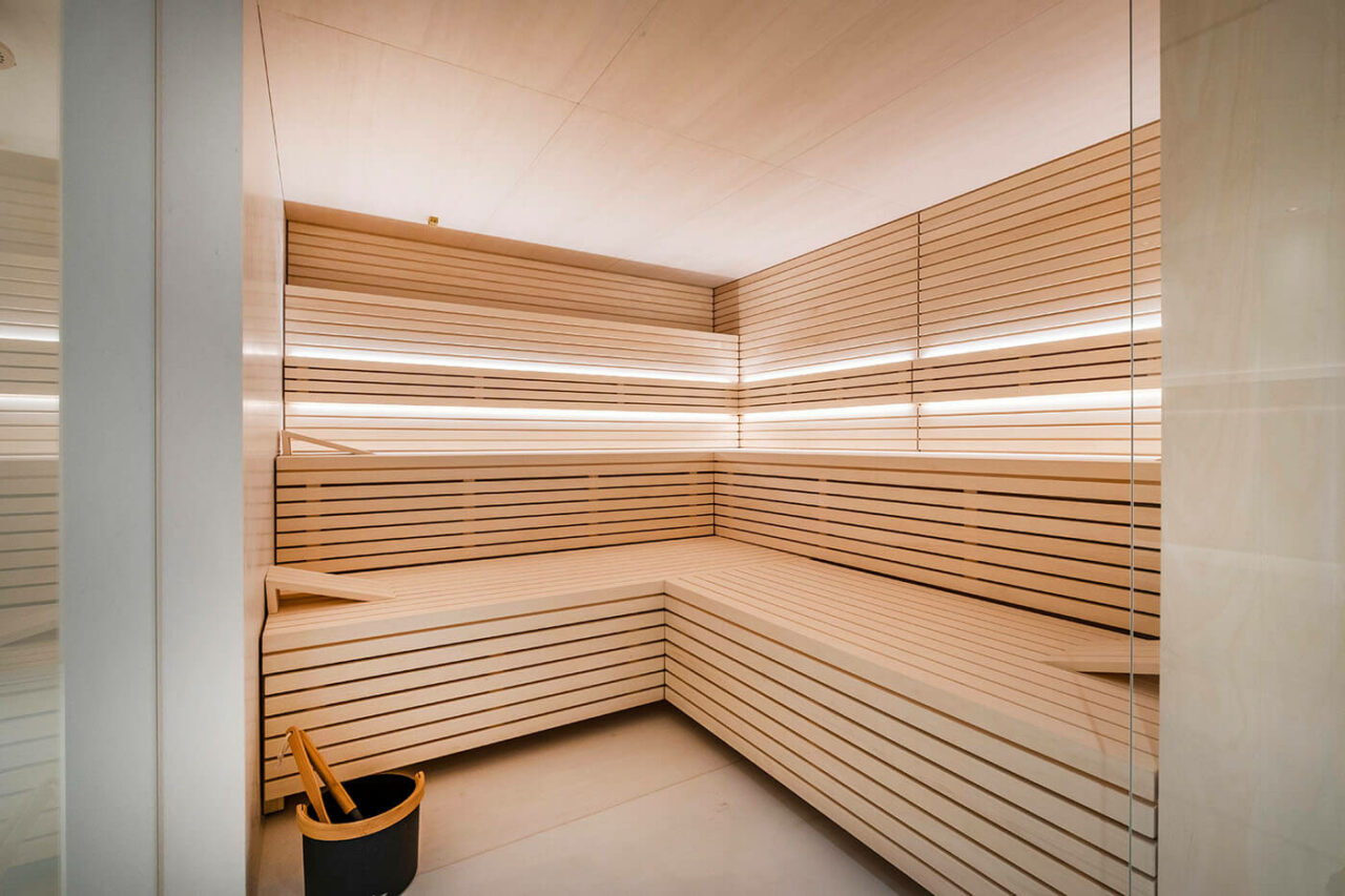 Sauna design lumineux avec poêle derrière banquettes 3 Design Sauna im Bauhausstil mit Hinterwandofen. Saunaholz: helle Espe in Stäbchenoptik. Große Glasfront, LED Beleuchtung, Hinterwandofen.