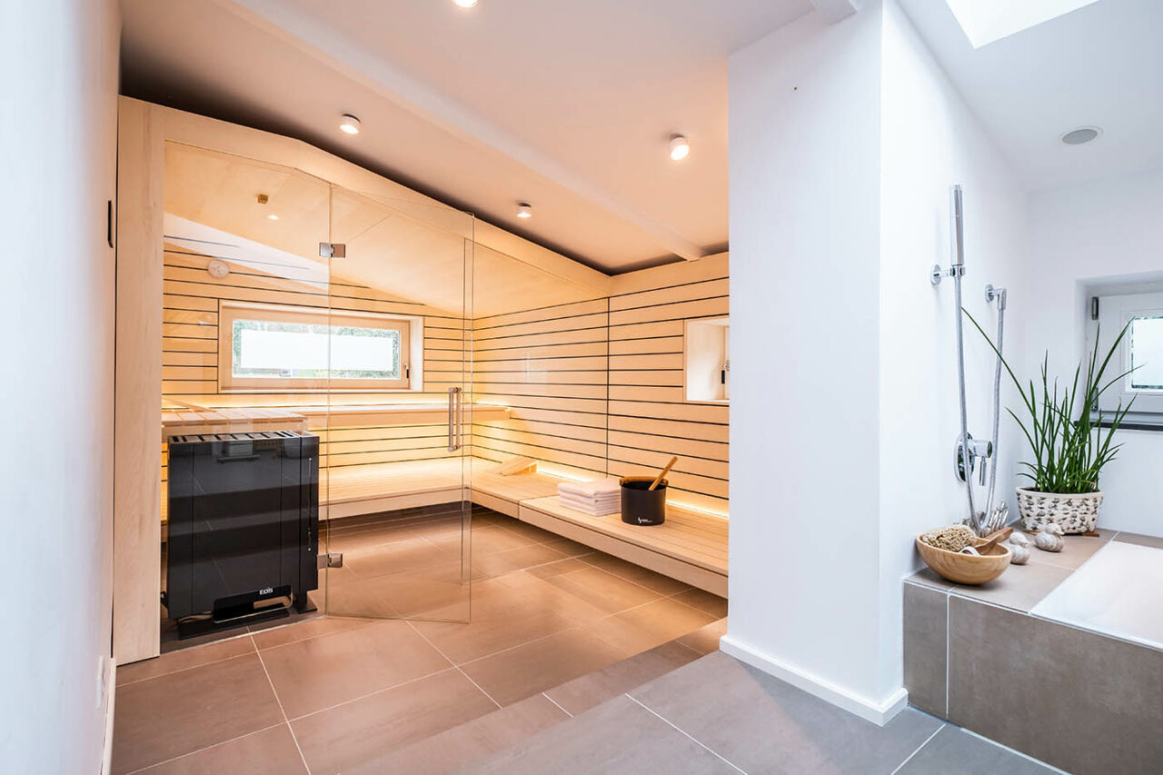 Sauna mit Fenster nach draußen 4 Design Sauna mit Fenster nach draußen. Sauna mit Dachschräge nach Maß in hellem Holz. Große Glasfront, nach außen verlängerte Bänke und LED Beleuchtung. Frei stehender Saunaofen und schwebende Saunabänke.