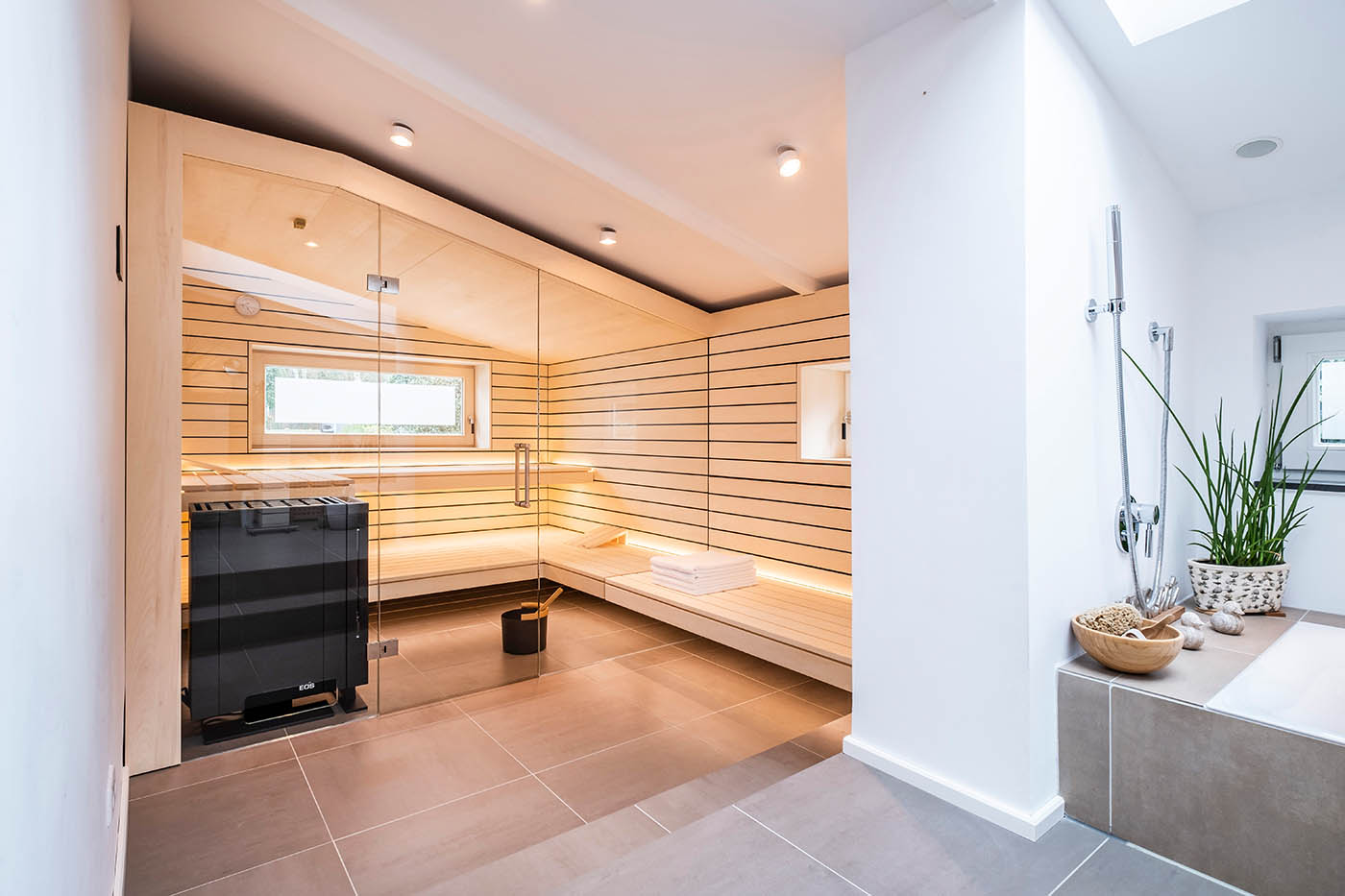 Sauna mit Fenster nach draußen 23 Design Sauna mit Fenster nach draußen. Sauna mit Dachschräge nach Maß in hellem Holz. Große Glasfront, nach außen verlängerte Bänke und LED Beleuchtung. Frei stehender Saunaofen und schwebende Saunabänke.