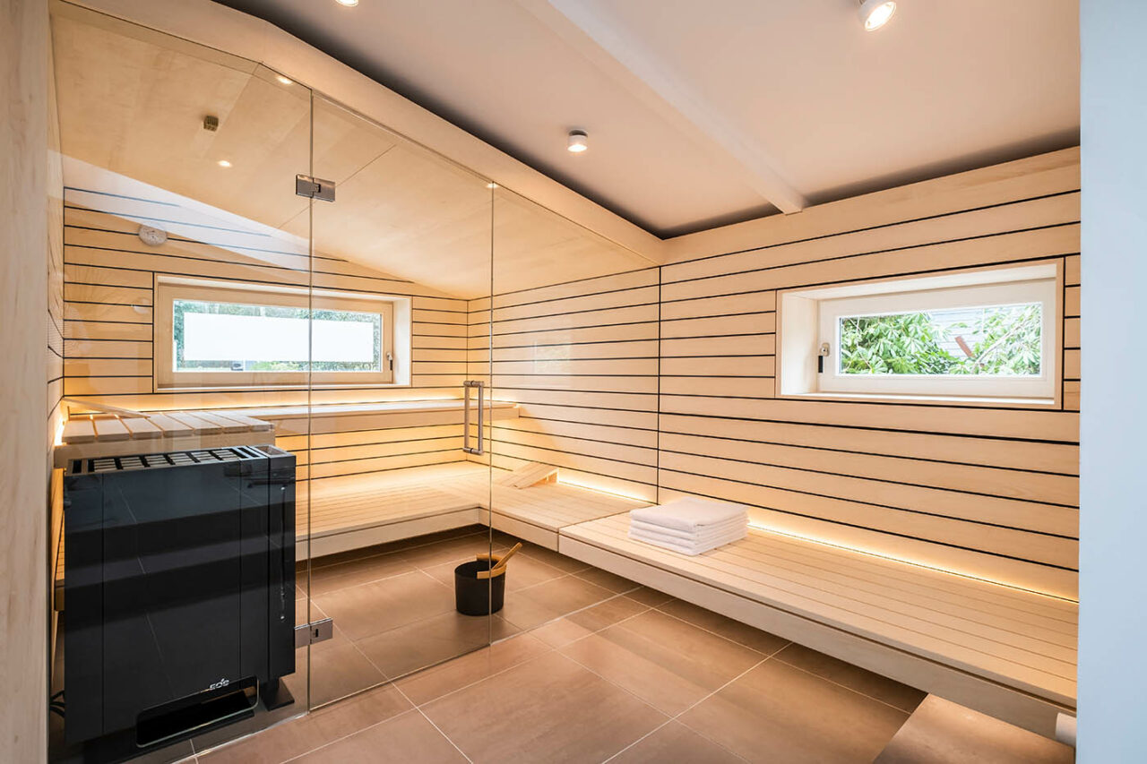 Sauna mit Fenster nach draußen 7 Design Sauna mit Fenster nach draußen. Sauna mit Dachschräge nach Maß in hellem Holz. Große Glasfront, nach außen verlängerte Bänke und LED Beleuchtung. Frei stehender Saunaofen und schwebende Saunabänke.
