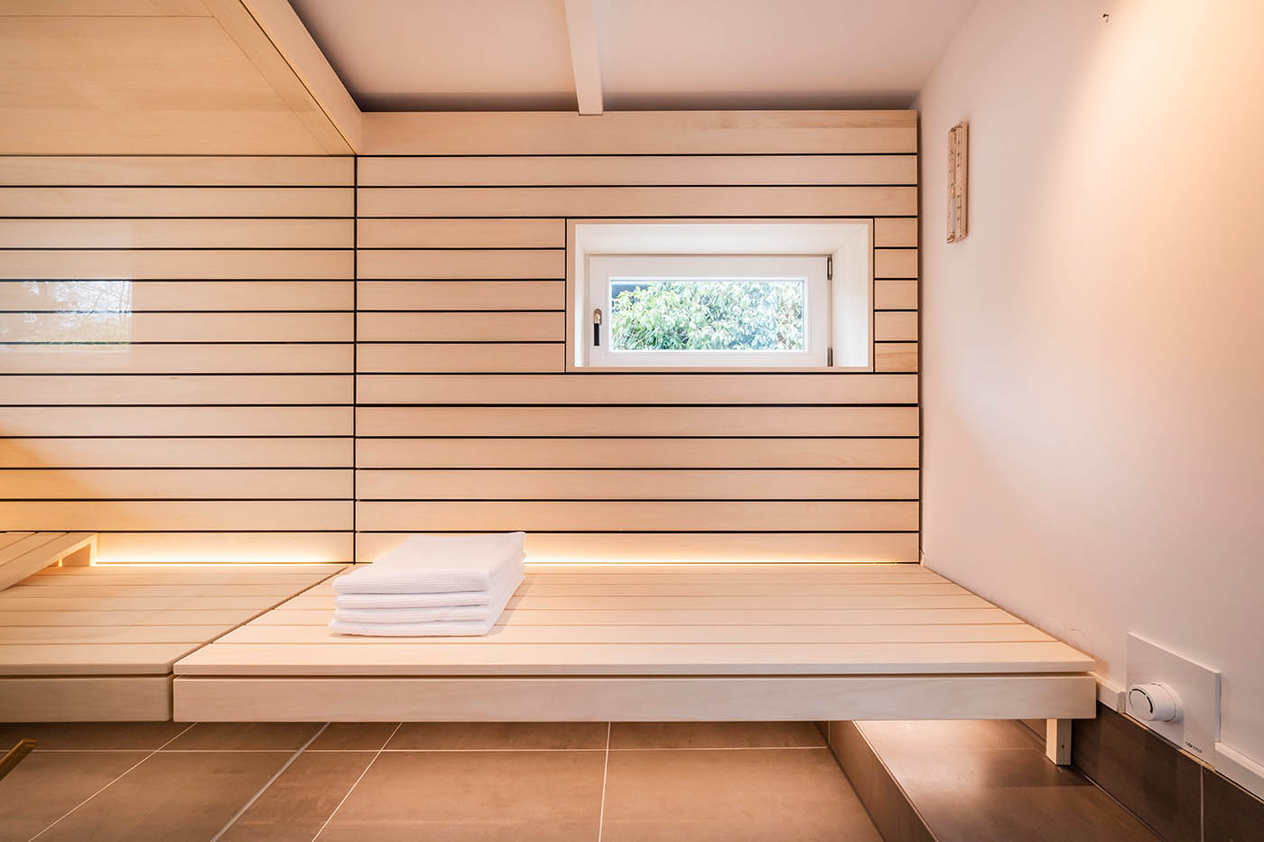 Sauna mit Fenster nach draußen 27 Design Sauna mit Fenster nach draußen. Sauna mit Dachschräge nach Maß in hellem Holz. Große Glasfront, nach außen verlängerte Bänke und LED Beleuchtung. Frei stehender Saunaofen und schwebende Saunabänke.