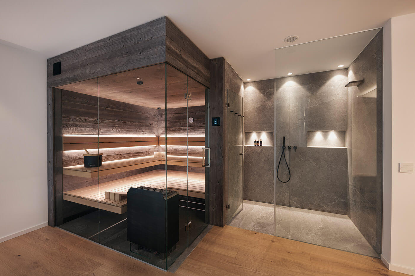 Service + FAQ Saunatechnik 6 Sauna nach Maß: Sauna in grauem Altholz mit großzügiger Verglasung, schwebenden Saunabänken vor der Glasfront und indirekter LED Beleuchtung. Maßanfertigung.